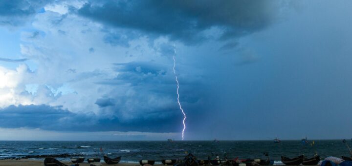 dramatic lightning strike over ocean and boat filled beach