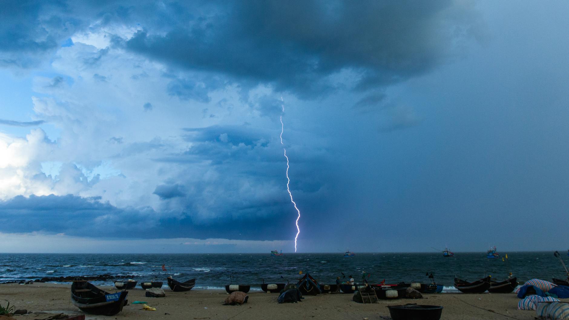 dramatic lightning strike over ocean and boat filled beach